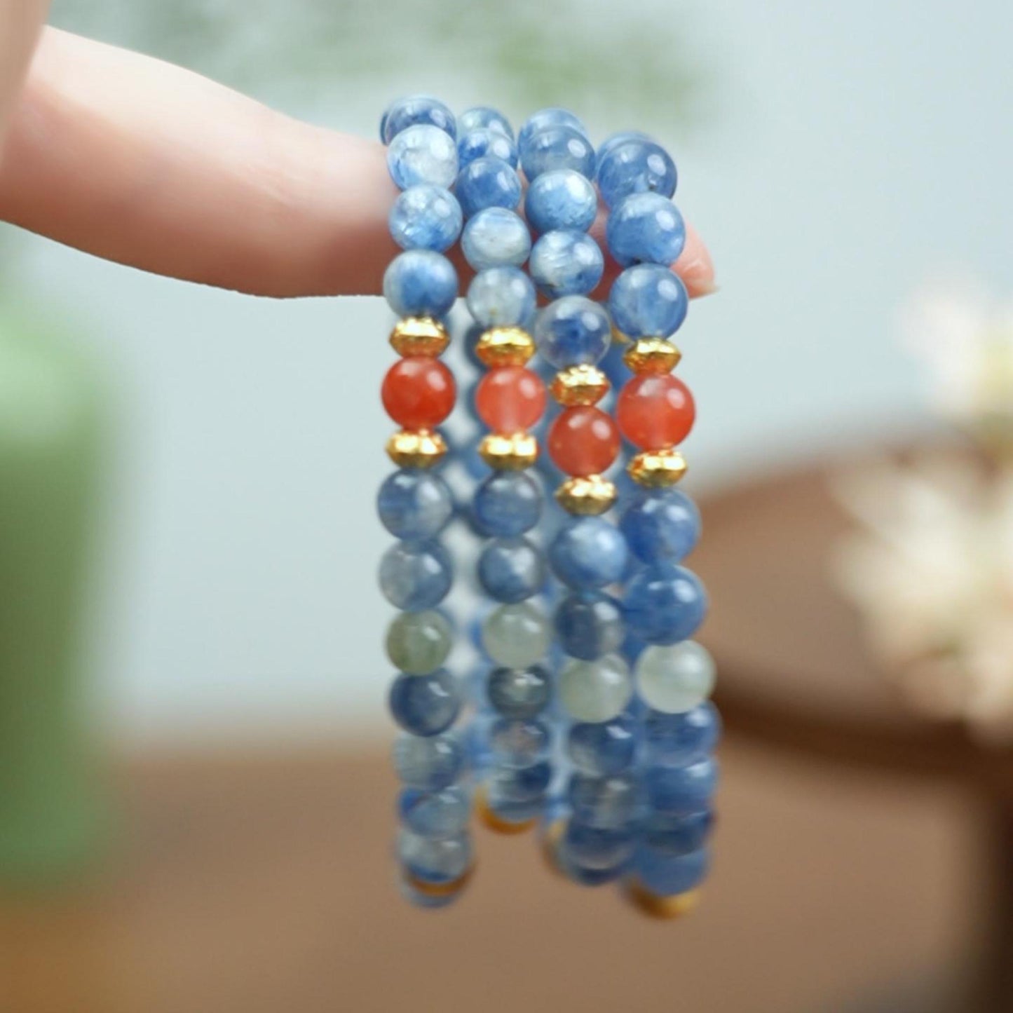 Hand holding coiled Triple Wrap Blue Kyanite bracelet with Red Agate and Tiger's Eye beads, Mala style jewelry