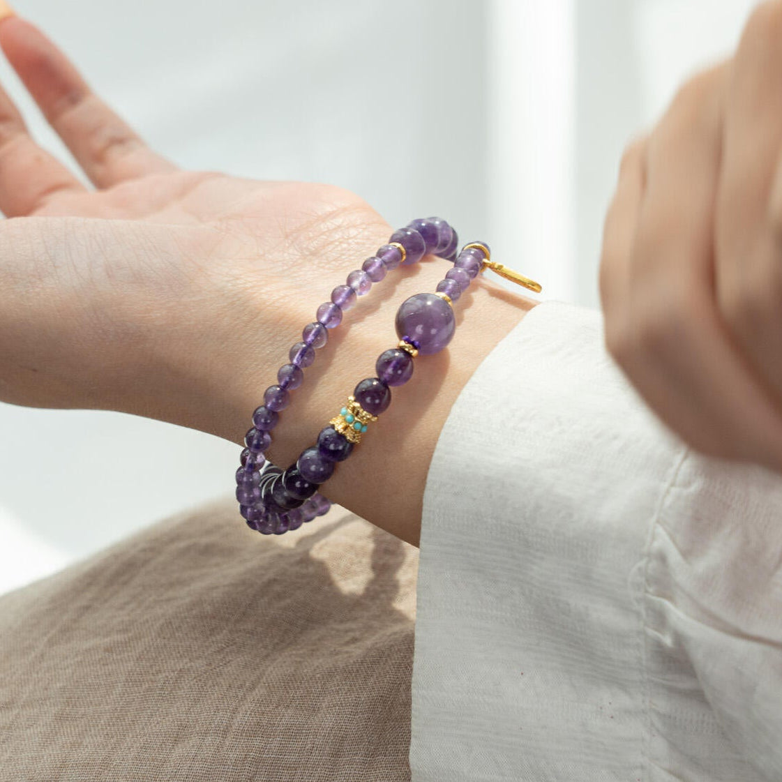 Woman wearing double wrap Amethyst Feng Shui bracelet on wrist showing gold spacers and protection tag