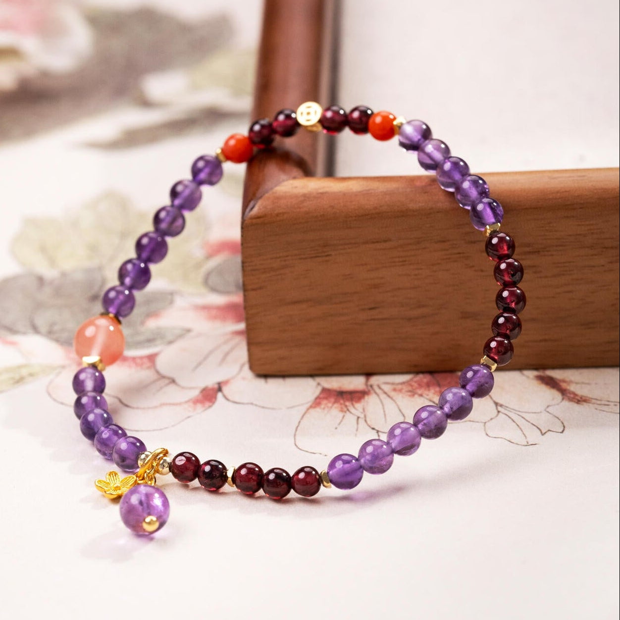 Dainty Amethyst and Garnet beaded bracelet featuring Southern Red Agate and a gold floral charm on a desk