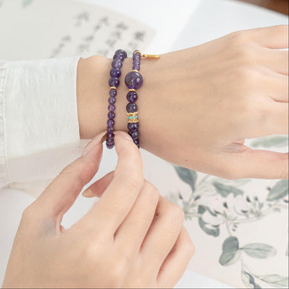 Hand holding Amethyst mala beads for meditation and mindfulness practice, showing the prominent Guru bead