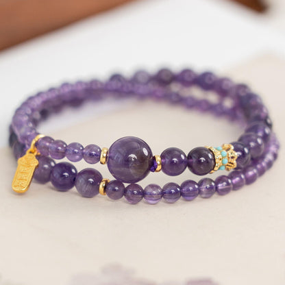 Genuine deep purple Amethyst 2-wrap mala bracelet featuring a gold amulet charm and turquoise accent bead close up