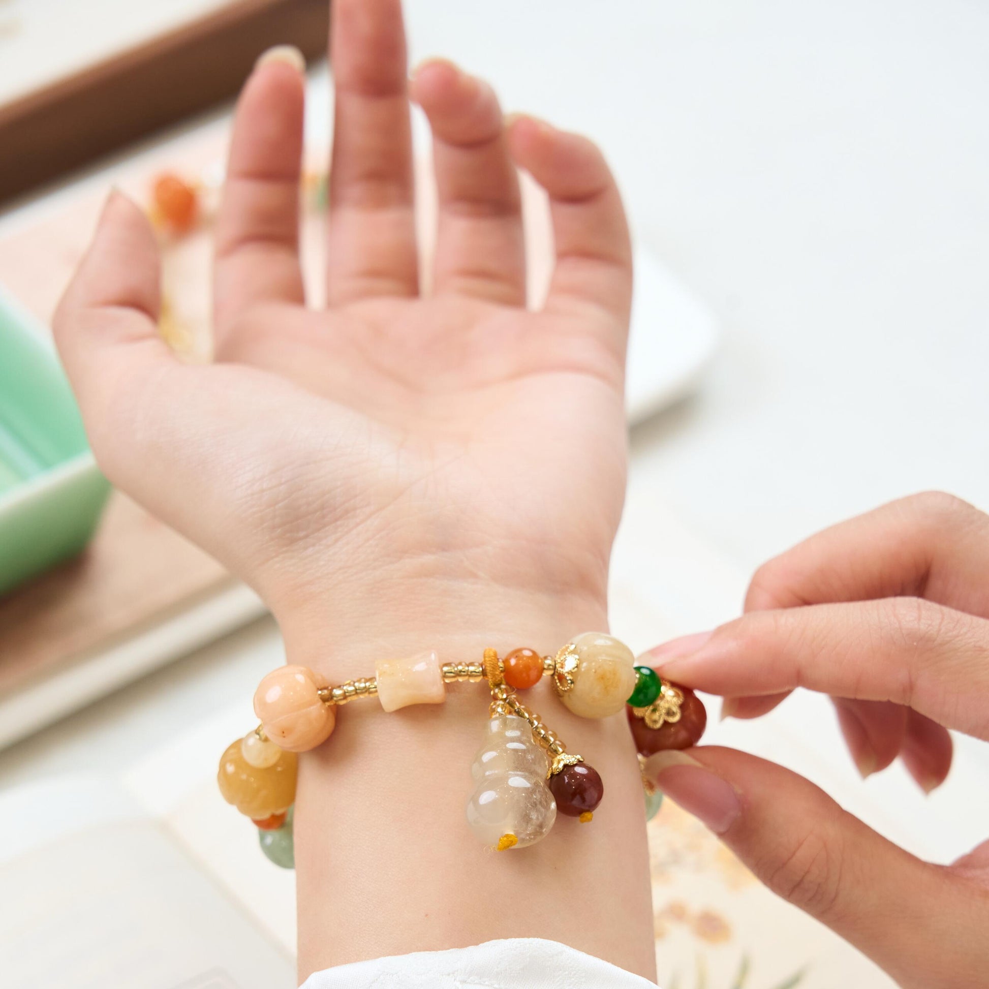 Woman wearing Golden Silk Jade bracelet featuring carved pumpkin beads and a dangling Feng Shui Gourd charm for good luck