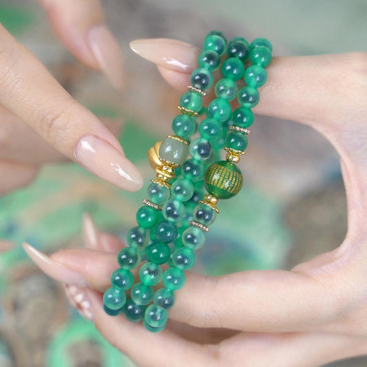 Woman wearing 3-wrap green agate mala bracelet with gold lotus pod charm and Hetian jade spacer