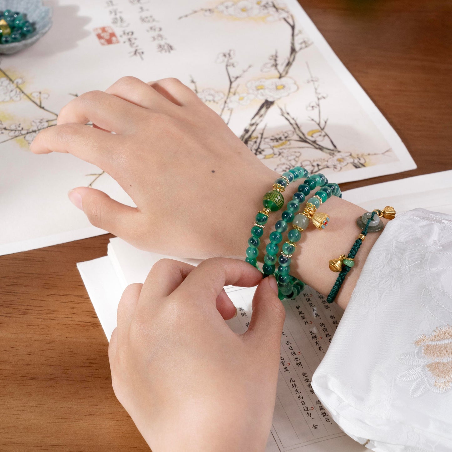 Hand resting on book wearing green healing crystal bracelet, symbolizing mindfulness and spiritual growth