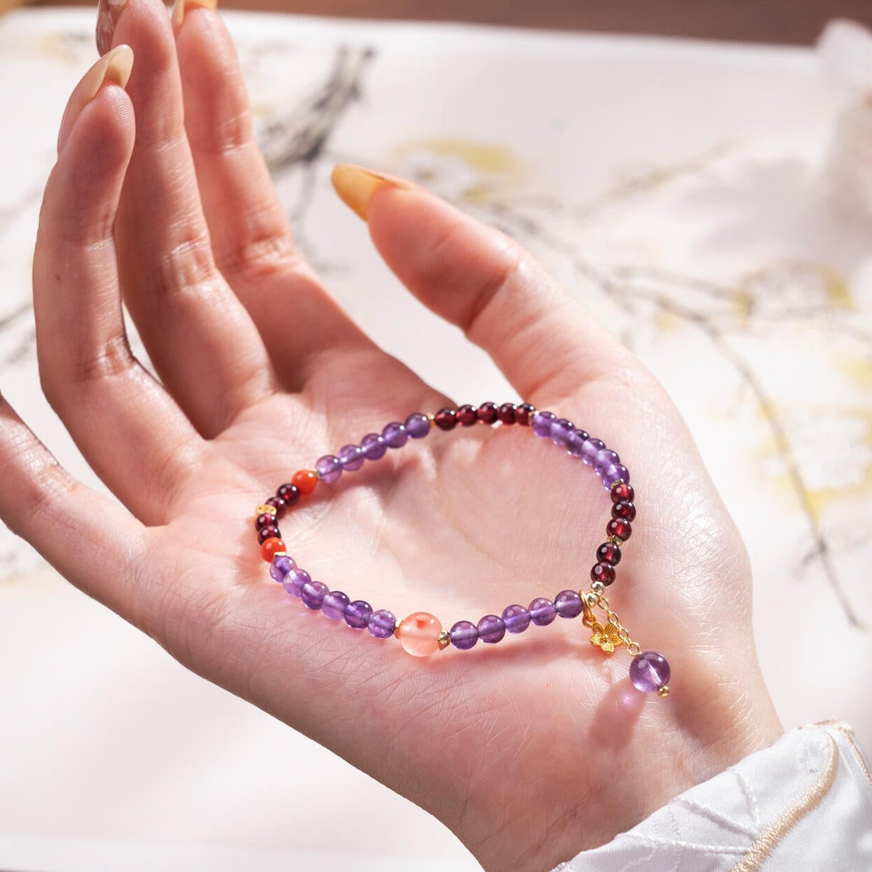 Hand holding multi-gemstone bracelet showing deep red Garnet and purple Amethyst beads for Chakra balancing