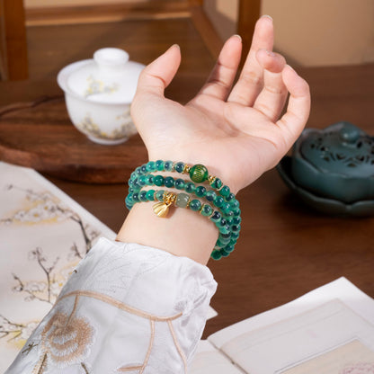 Close up of translucent Sugar Heart Agate beads on wrist, showing the unique green texture and gold bell charm