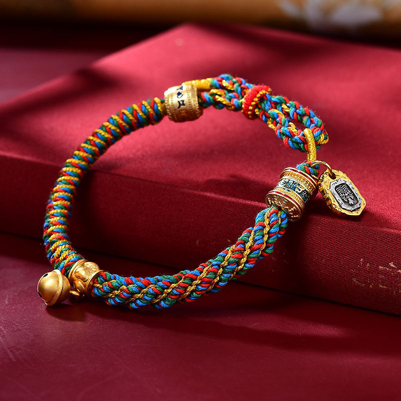 Close up of gold-tone mantra barrel bead and enamel details on a handmade rope bracelet
